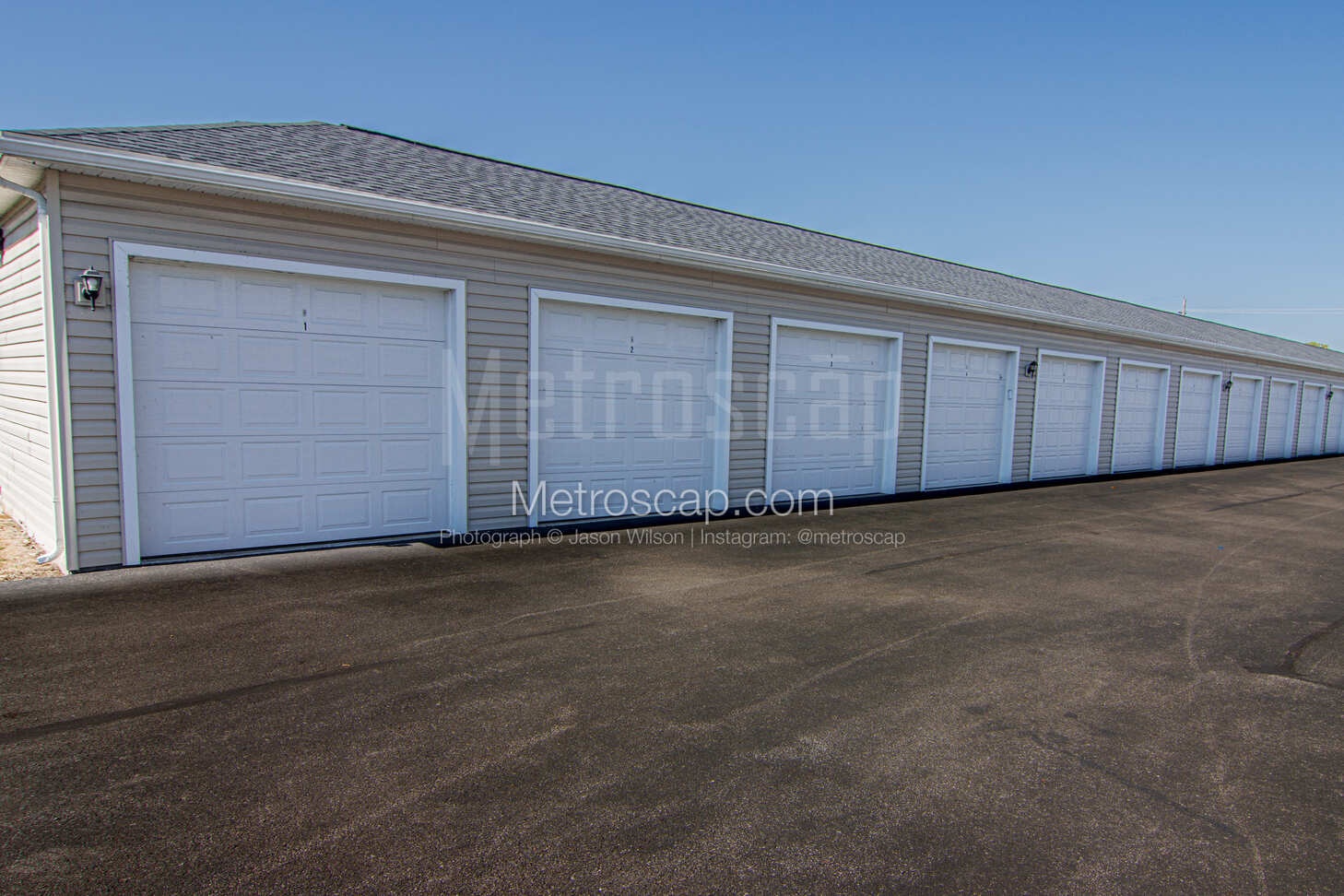 A long row of detached or individual garages with white doors and gray siding